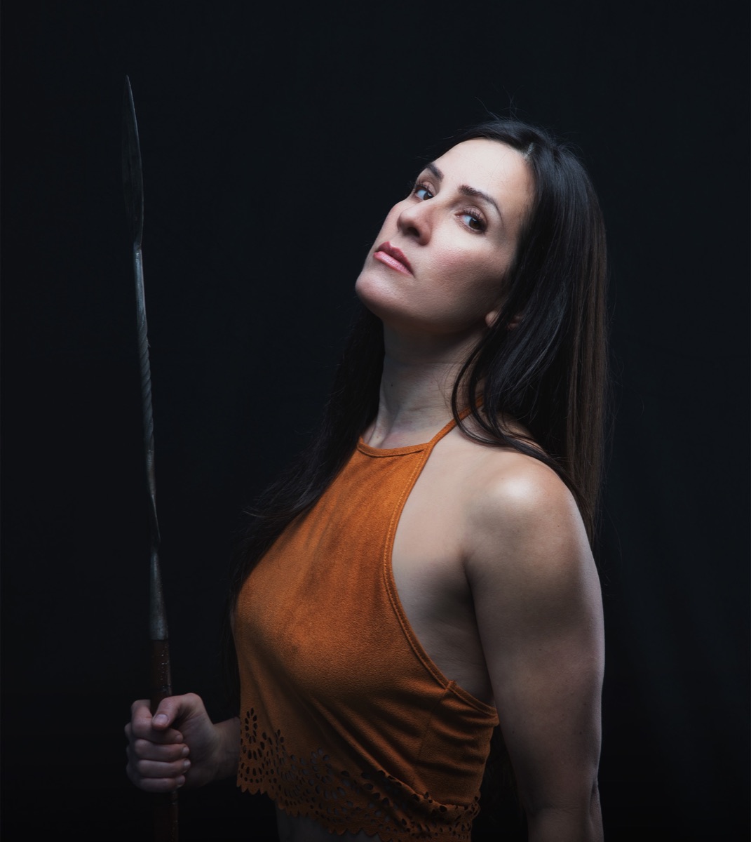 A strong woman holding a spear, lit dramatically