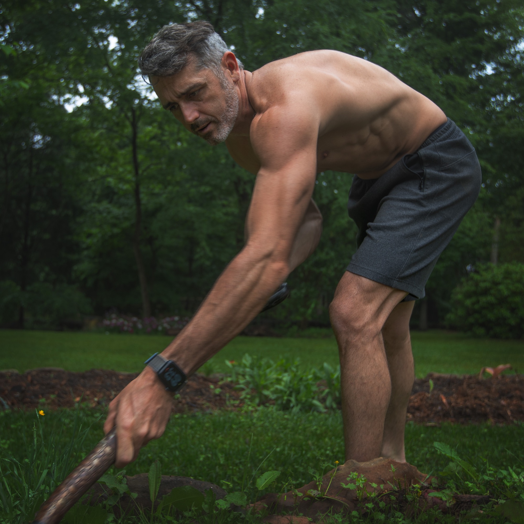 A lean, muscular man working the earth with a wooden digging stick