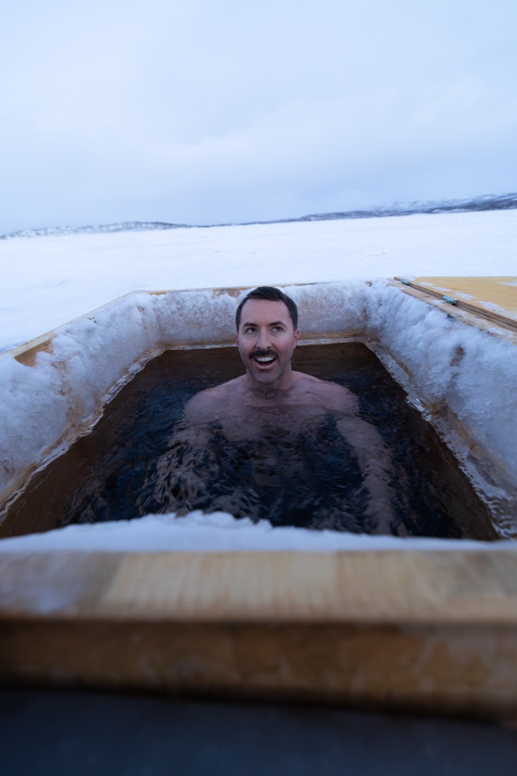 A smiling man chest-deep in an ice bath cut into a frozen lake