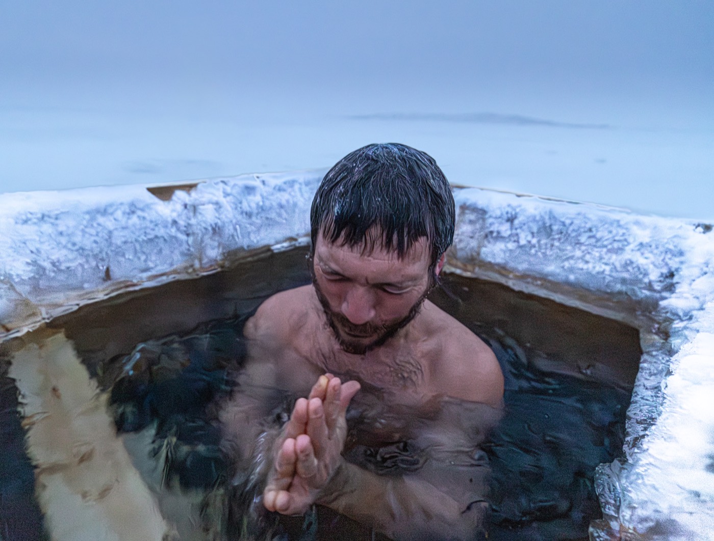A man steadying his breath in the ice water at dusk