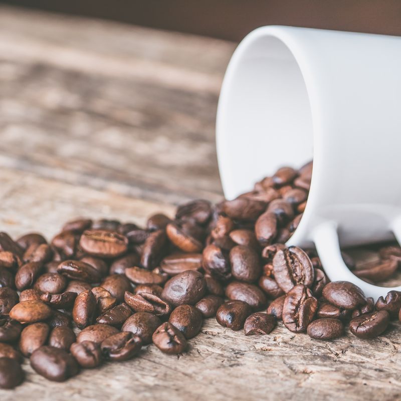 Coffee beans spilling from a white mug onto a wooden table